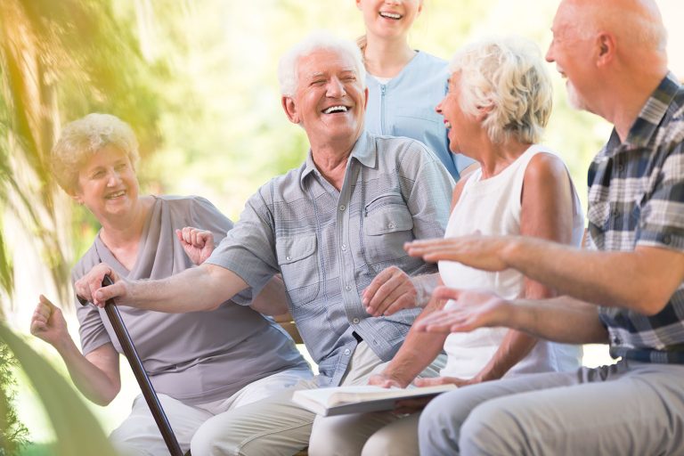Group of smiling senior friends enjoying time while sitting together in park